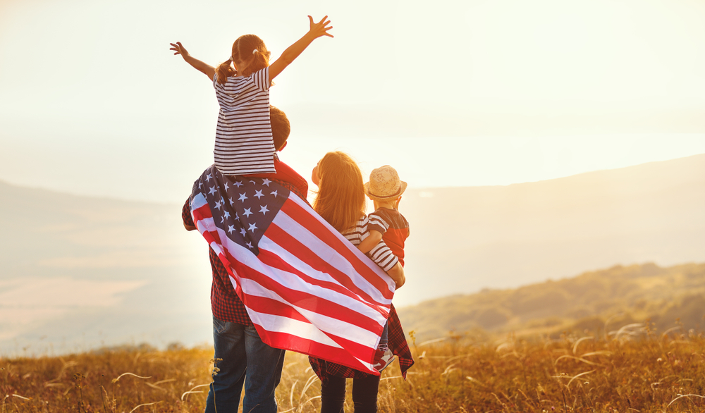 A cheerful American family with children waving the U.S. flag outdoors, symbolizing national pride and the spirit of freedom.